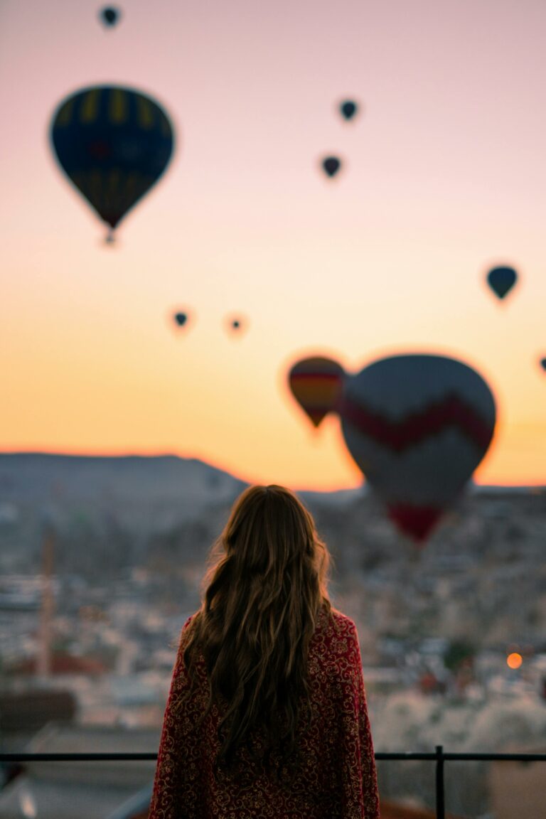 A woman watches hot air balloons at sunrise in Cappadocia, Turkey, creating a breathtaking view.