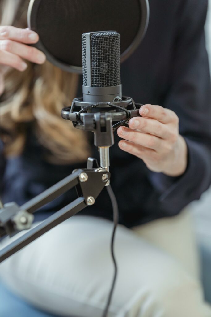 Hands adjusting a studio microphone with a pop filter in an indoor setting.