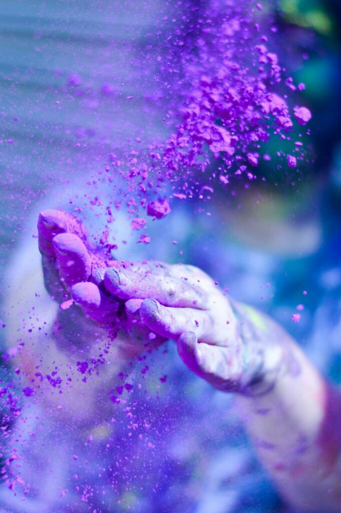Close-up of hands throwing vibrant purple powder outdoors, capturing motion and color.