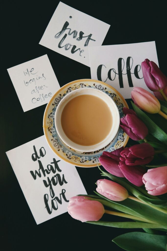 A cup of coffee with motivational notes and vibrant tulips on a dark table.