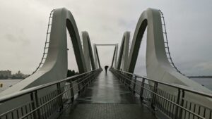 A solitary figure walks across an iconic modern bridge in Kyiv, Ukraine, against a moody sky.