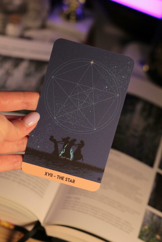 Close-up of Tarot 'The Star' card held over open book, indoors.