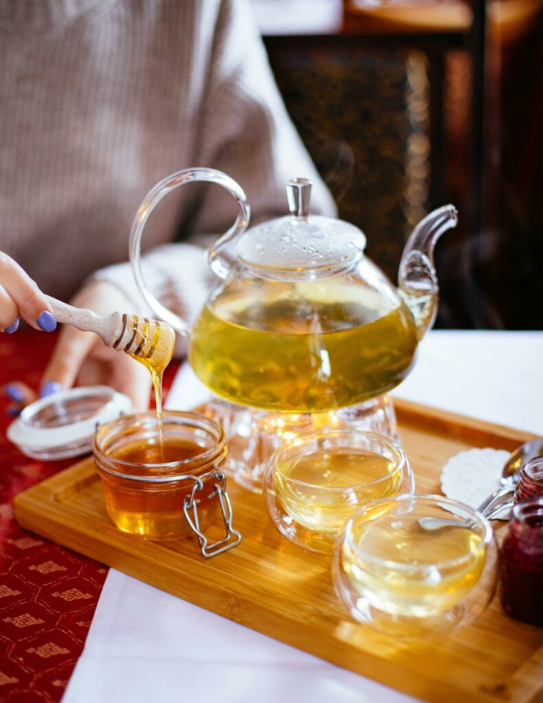 A cozy scene of honey being added to steaming herbal tea in a glass teapot, perfect for relaxation.