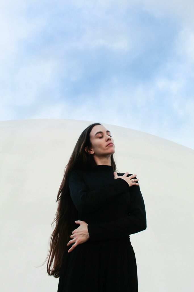 Serene portrait of a woman embracing herself against a minimalist sky background.