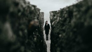 A woman with brown hair stands between rocky walls on a windy, cloudy day.