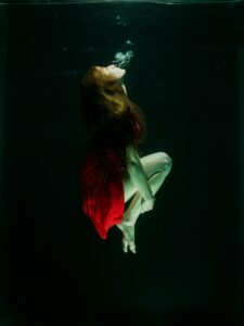 Woman in red dress captured gracefully underwater, creating an ethereal and artistic scene.