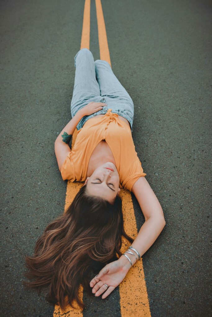 A woman in casual attire laying on a road with vibrant yellow lines, showcasing fashion and style.
