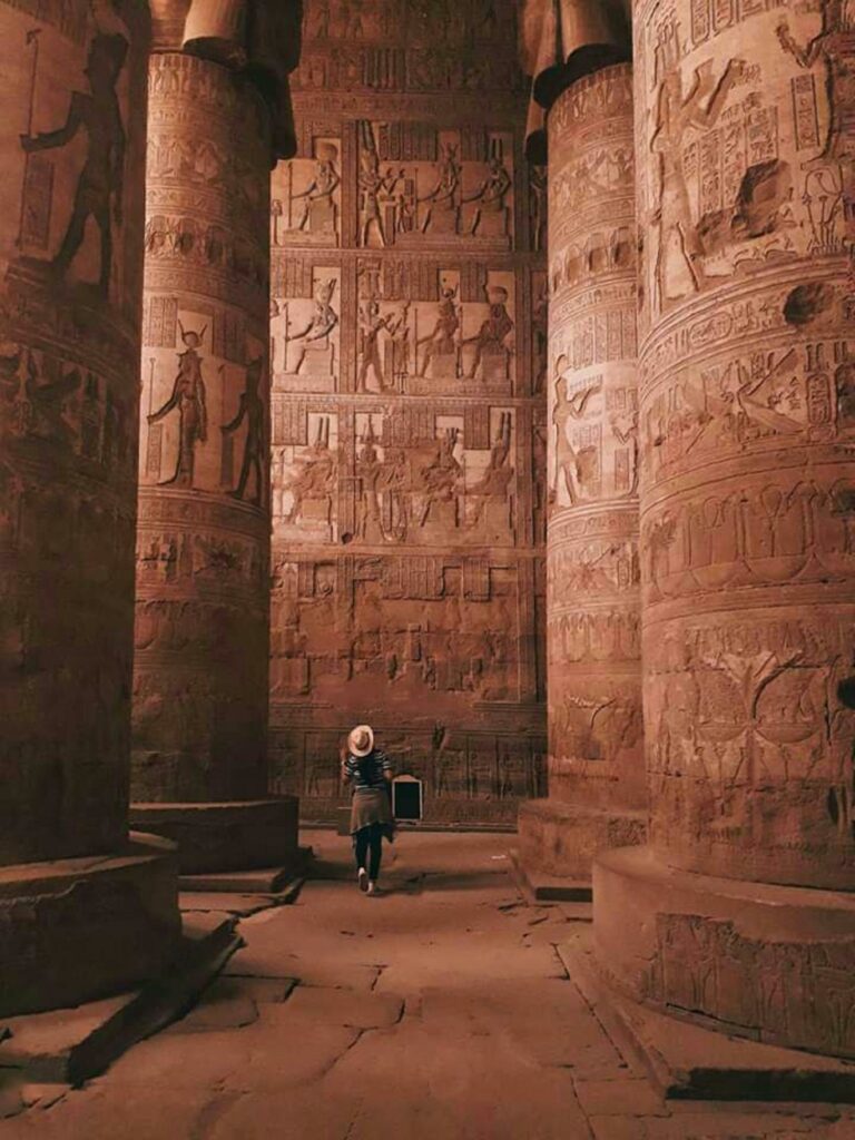 Tourist exploring the intricately carved columns of Dendera Temple, Egypt.