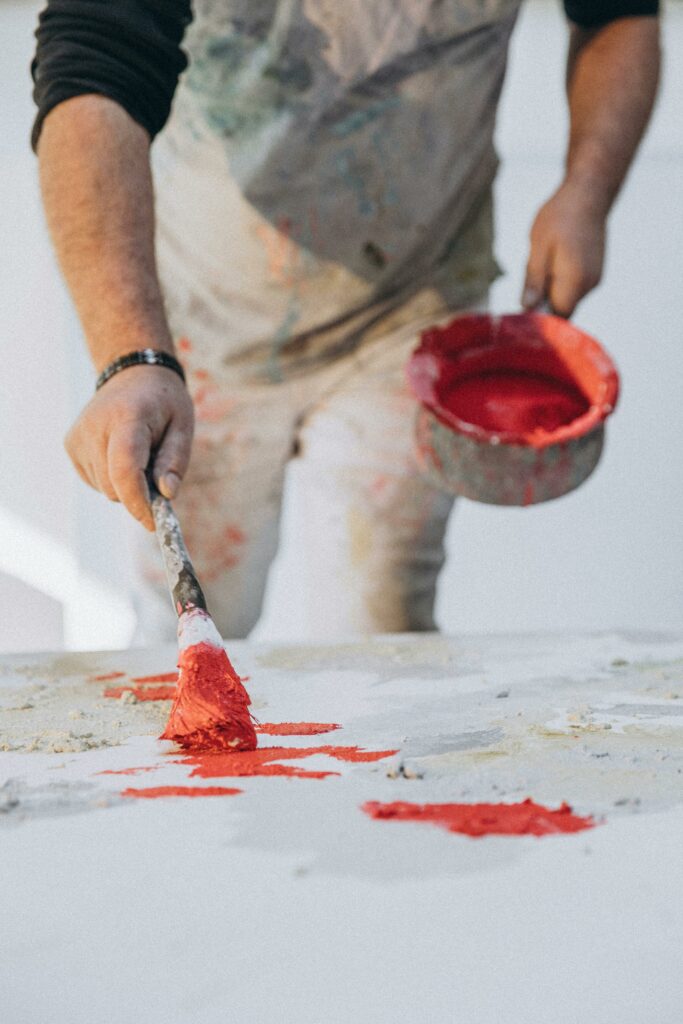 Close-up of an artist applying vibrant red paint on a canvas in a studio setting.