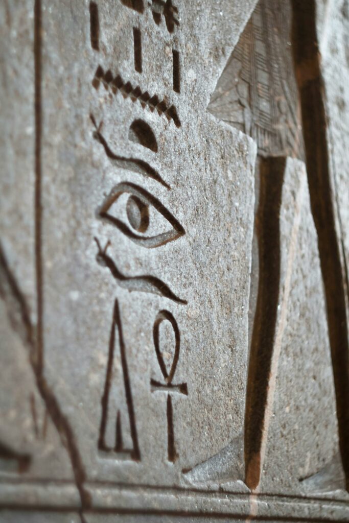 Detailed close-up of hieroglyphs on sandstone in Paris exhibit, highlighting ankh and eye symbols.