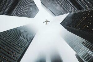 Airplane soaring above fog-enshrouded skyscrapers in an urban setting.