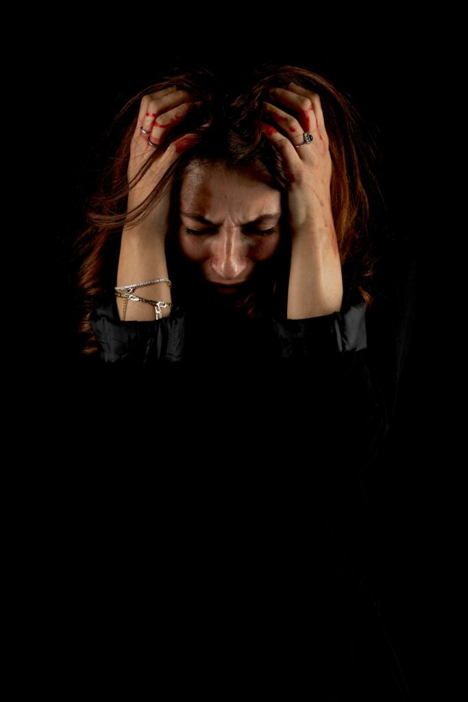 Woman holding head in distress against a dark background, symbolizing emotional struggle.