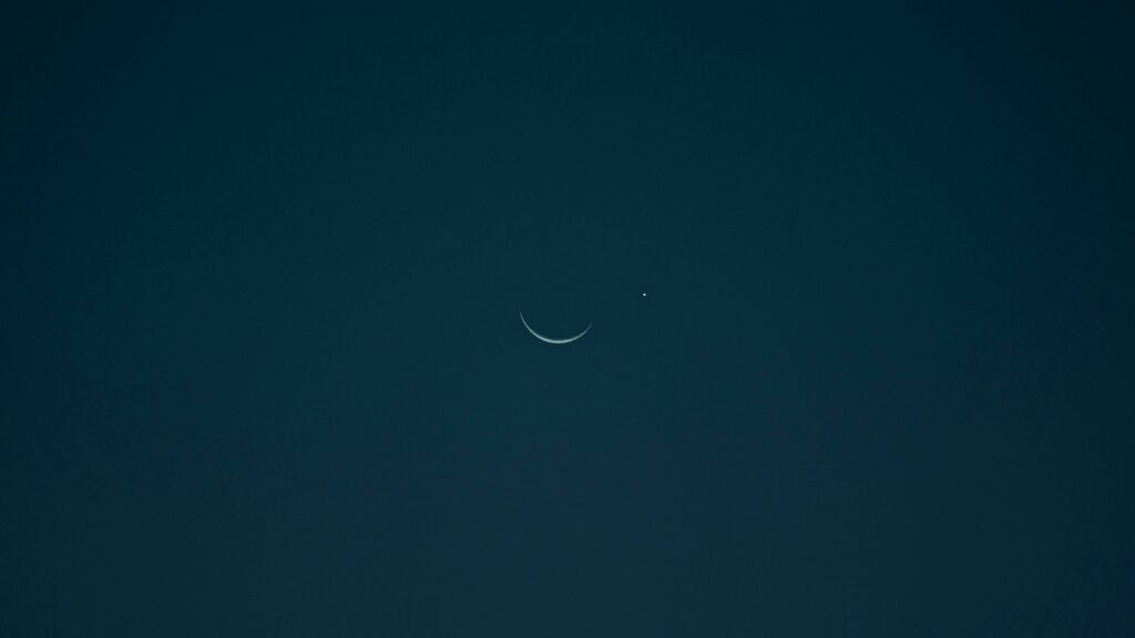 A serene crescent moon and bright planet set against a dark night sky.