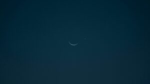 A serene crescent moon and bright planet set against a dark night sky.