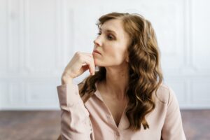 A thoughtful woman with curly hair sits indoors, reflecting deeply in a serene setting.