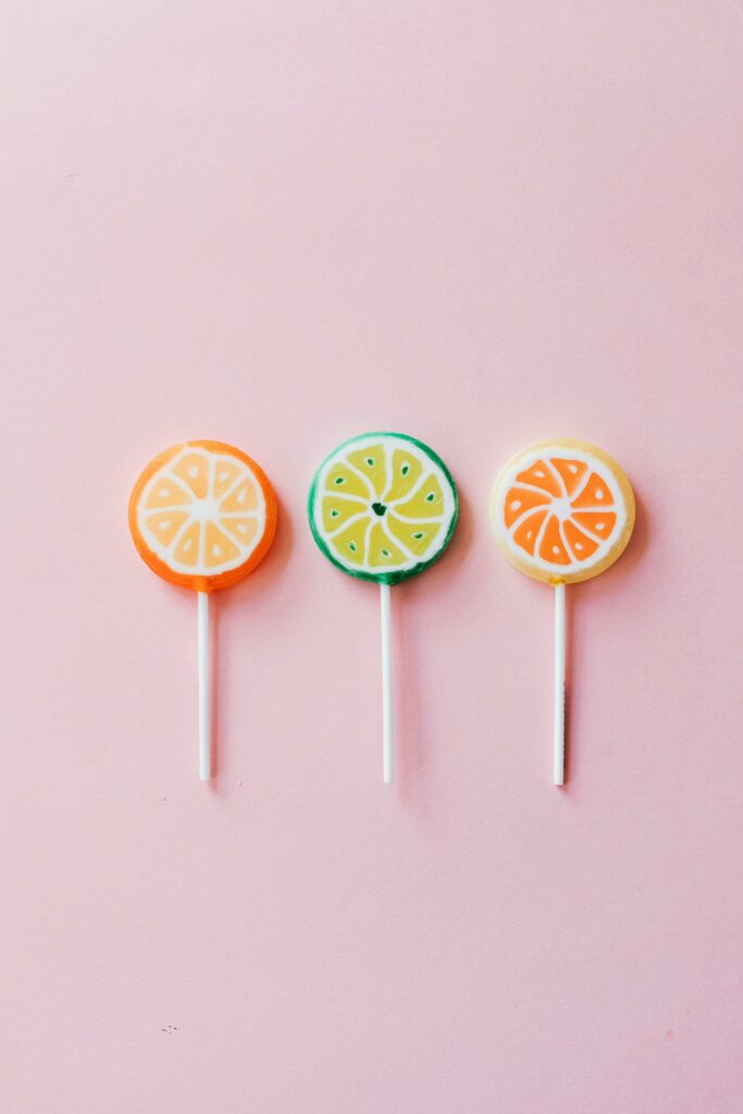 Three fruity lollipops arranged on a pink background, offering vibrant citrus hues.