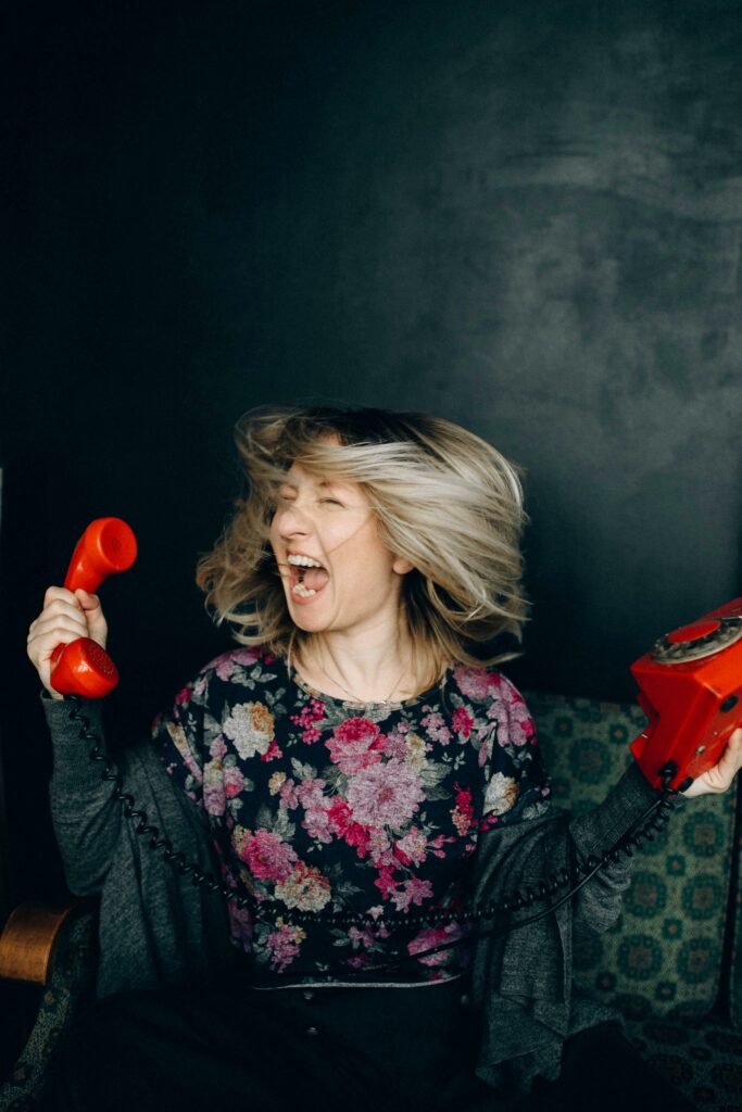 A woman angrily shouting into a vintage red telephone indoors.