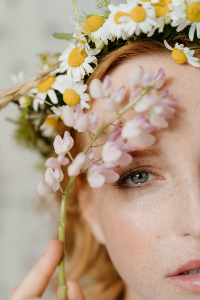 Close-up portrait of a redhead woman with a floral wreath featuring chamomile and wildflowers.