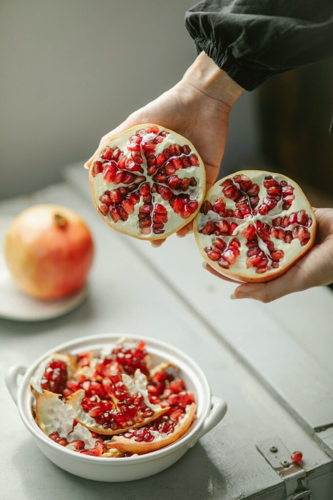 Vibrant pomegranate halves held above a bowl fill the frame, showcasing fresh, juicy seeds.