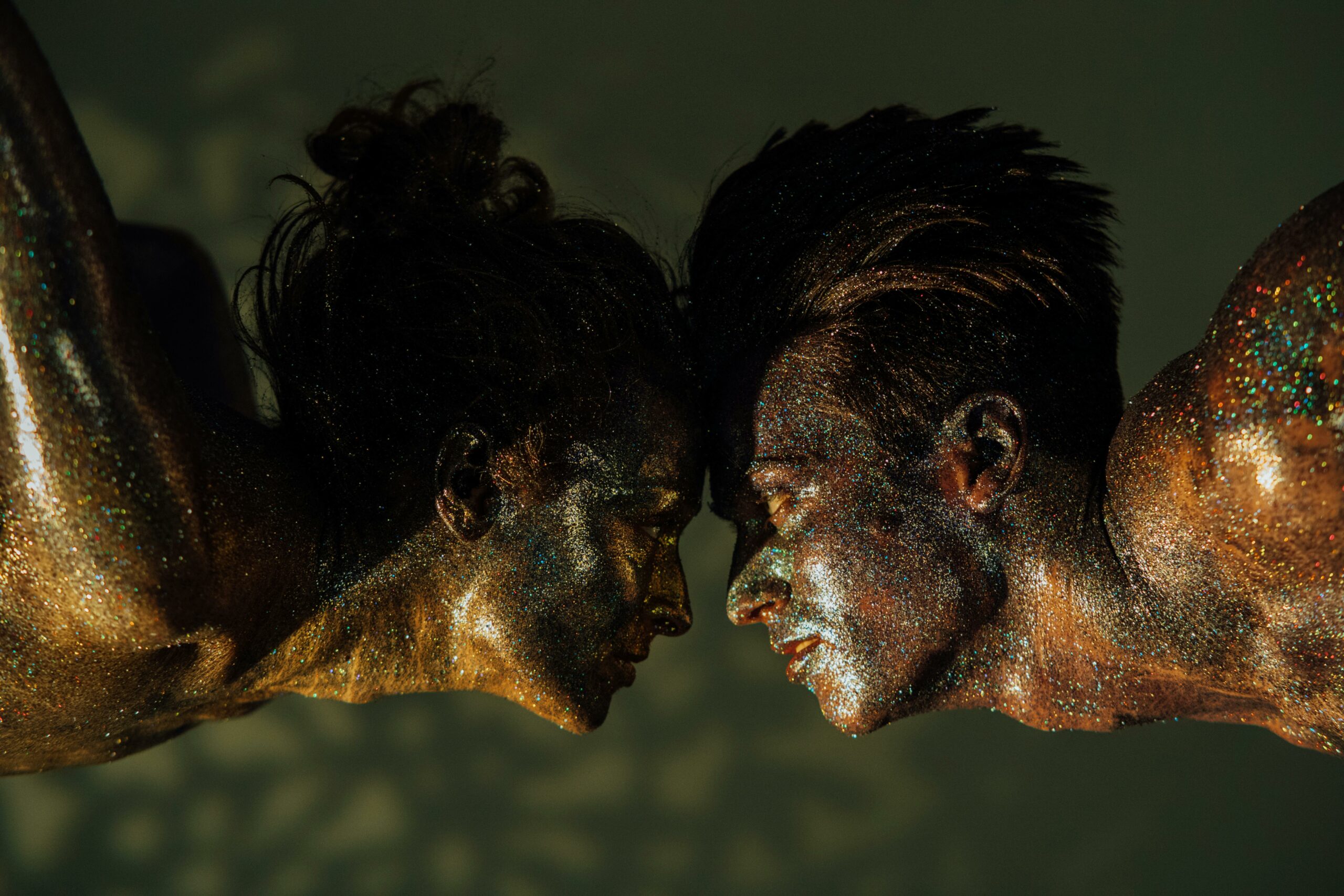 Close-up artistic portrait of two glitter-covered dancers in an intimate pose.