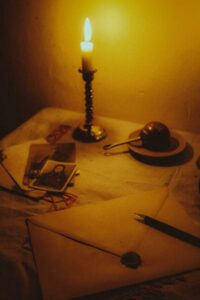 A vintage still life featuring a candlelit desk with a sealed envelope, fountain pen, and old photographs.