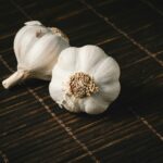 Two fresh garlic bulbs on a dark wooden mat, highlighting aromatic culinary ingredients. pexels-photo-928251-928251