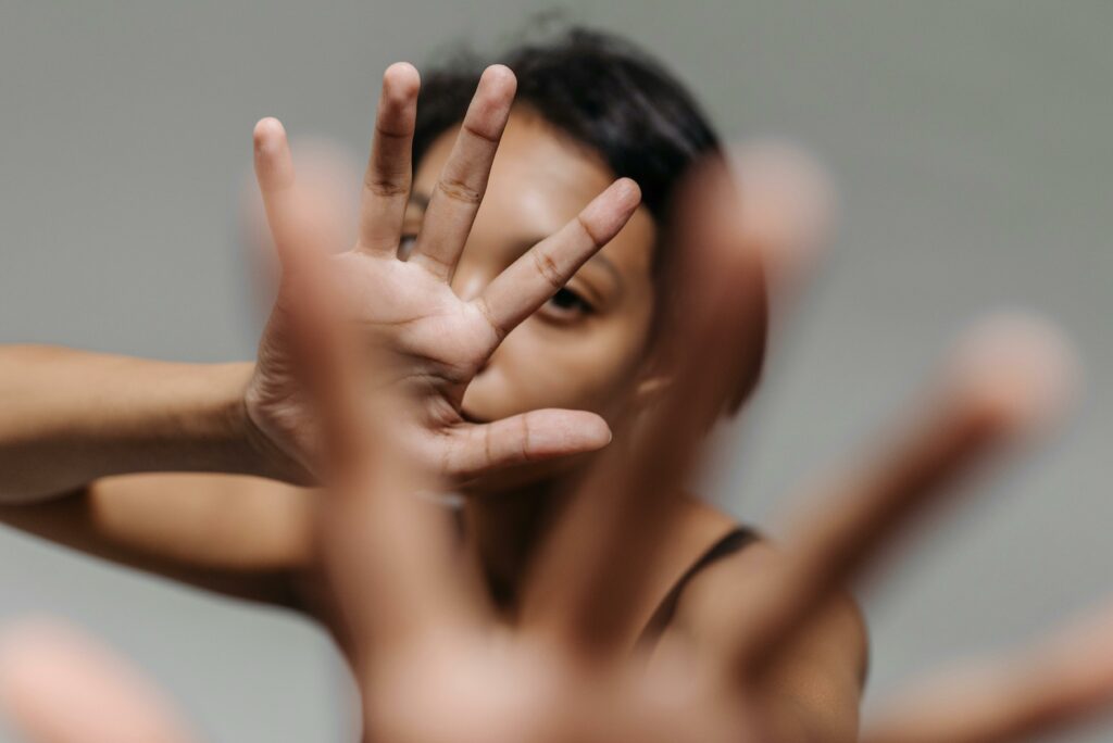 A woman uses hands to obscure her face against a gray backdrop.