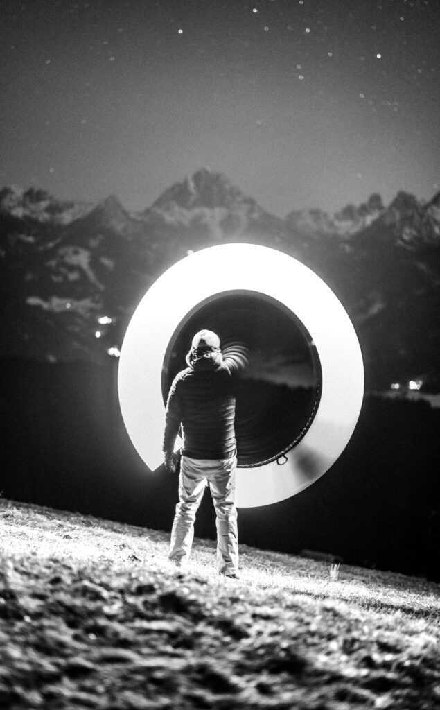 Silhouette with light ring under starlit sky in Italian mountains, creating a mystical scene.