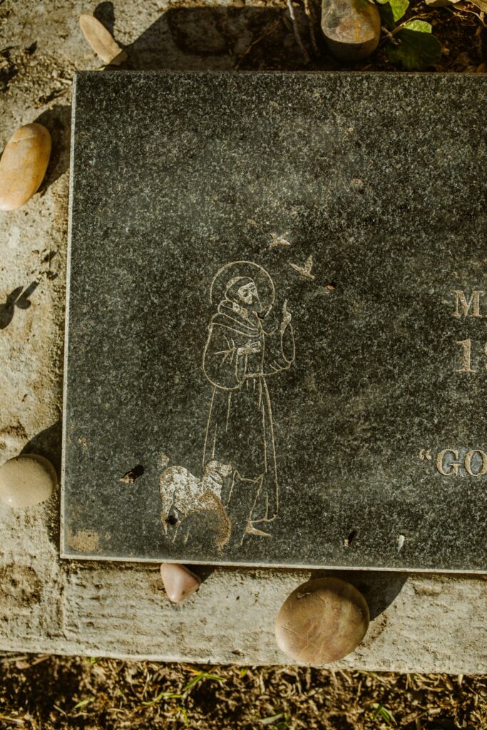 A textured gravestone featuring a saint and adorned with pebbles, symbolizing remembrance and serenity.