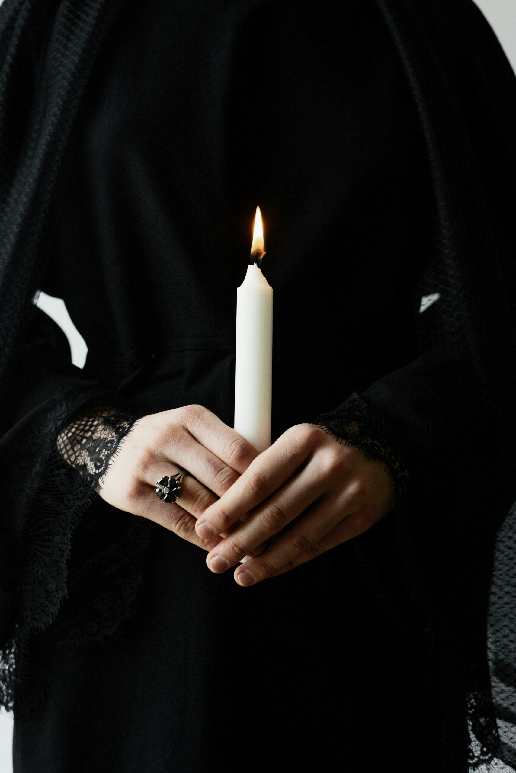 A person in dark clothing holds a burning candle, creating a moody yet serene ambiance.