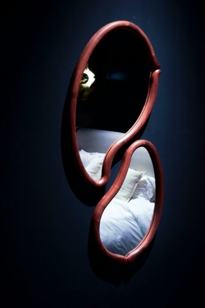 Artistic wall mirror with unique shape reflecting bedroom pillows.