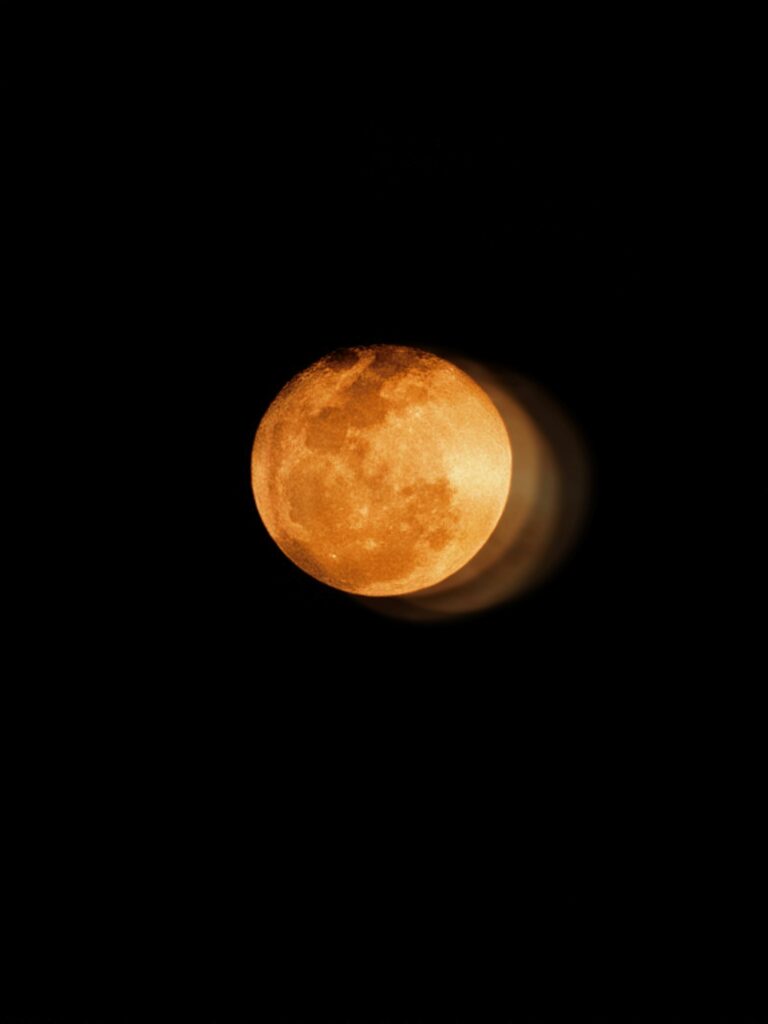 A captivating full moon with a golden hue against a dark, starless night sky.