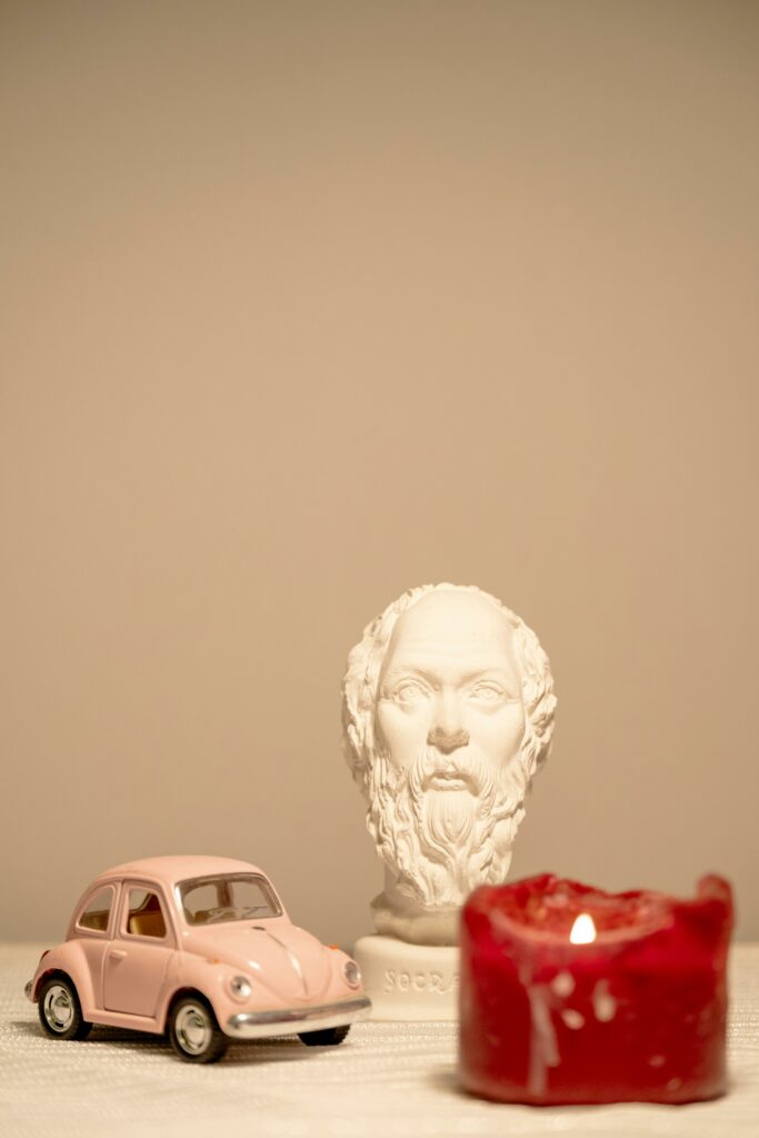 A serene still life with a bust, red candle, and vintage toy car.