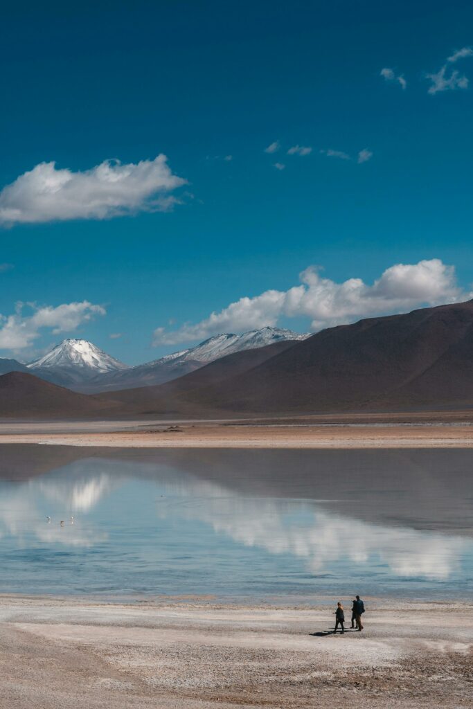 Two people walk across the famous Uyuni Salt Flats with stunning mountain views under a clear blue sky.