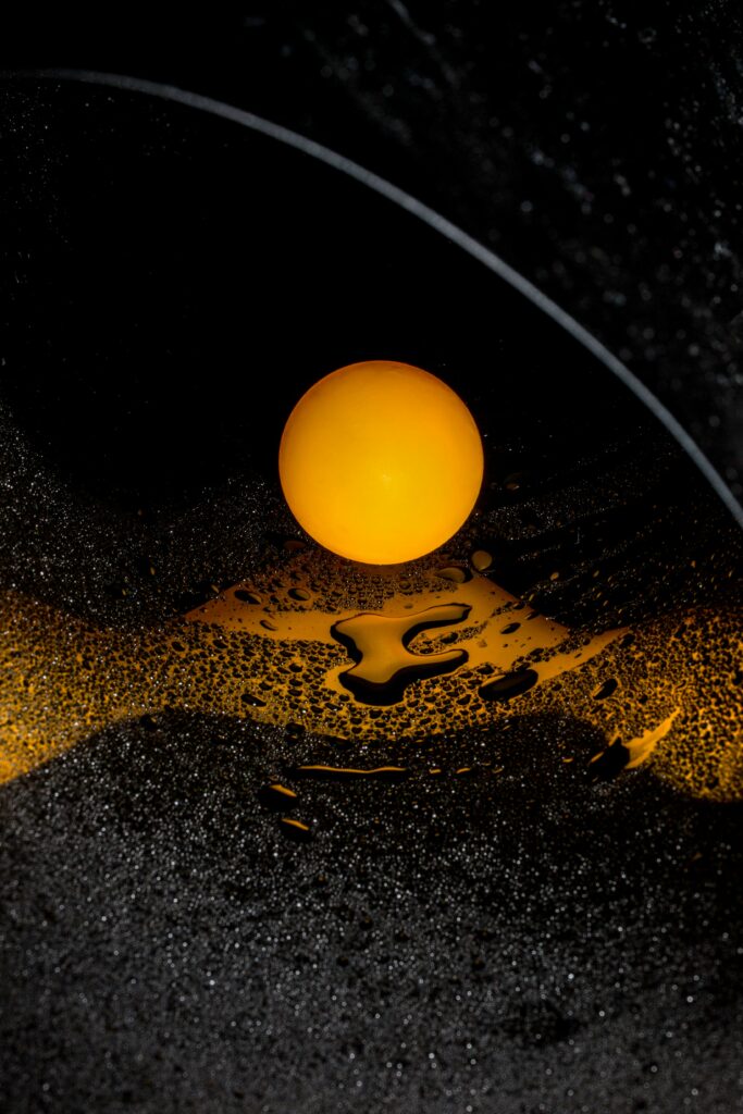 Artistic close-up of a single egg yolk on a textured black surface, showcasing its vibrant color.