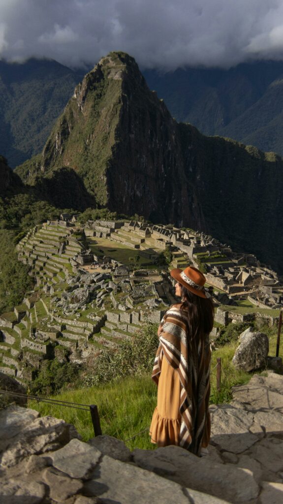 A woman in traditional attire gazes at Machu Picchu, creating a serene, cultural travel scene in Peru.