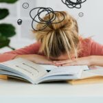 Young woman asleep over books at desk, conveying stress and mental overload. pexels-photo-6214833-6214833