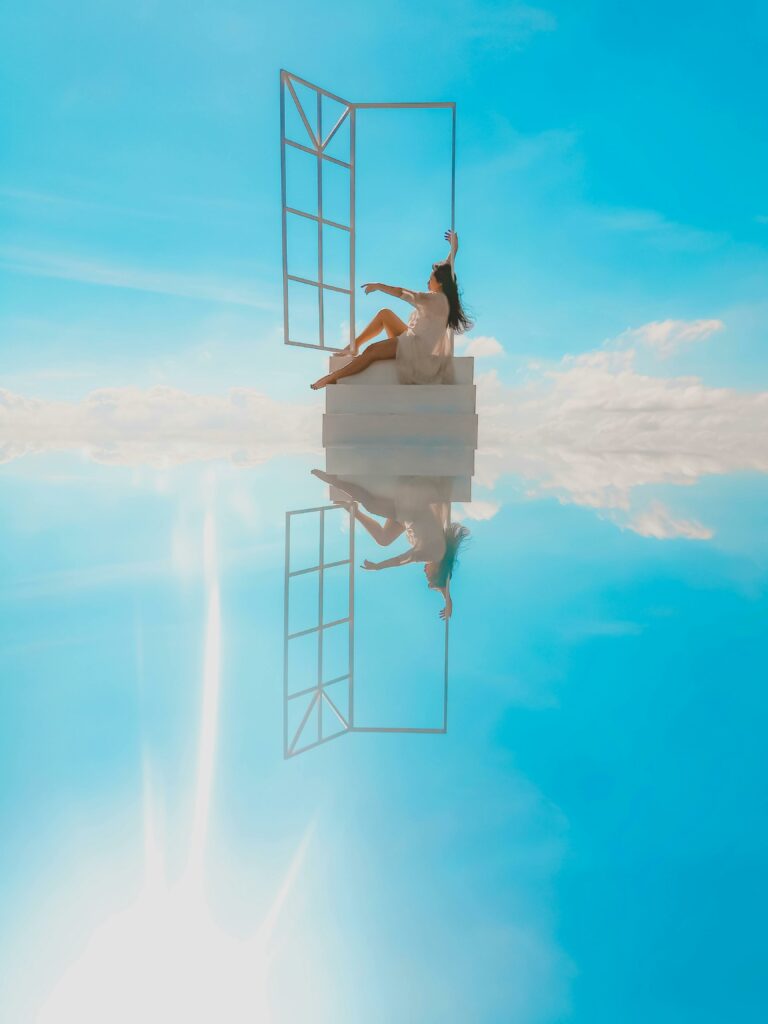 A woman in a white dress relaxes by an open window with a surreal reflection under a blue sky.
