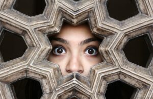 Close-up of a woman's eyes peering through a decorative lattice in New Delhi, India.