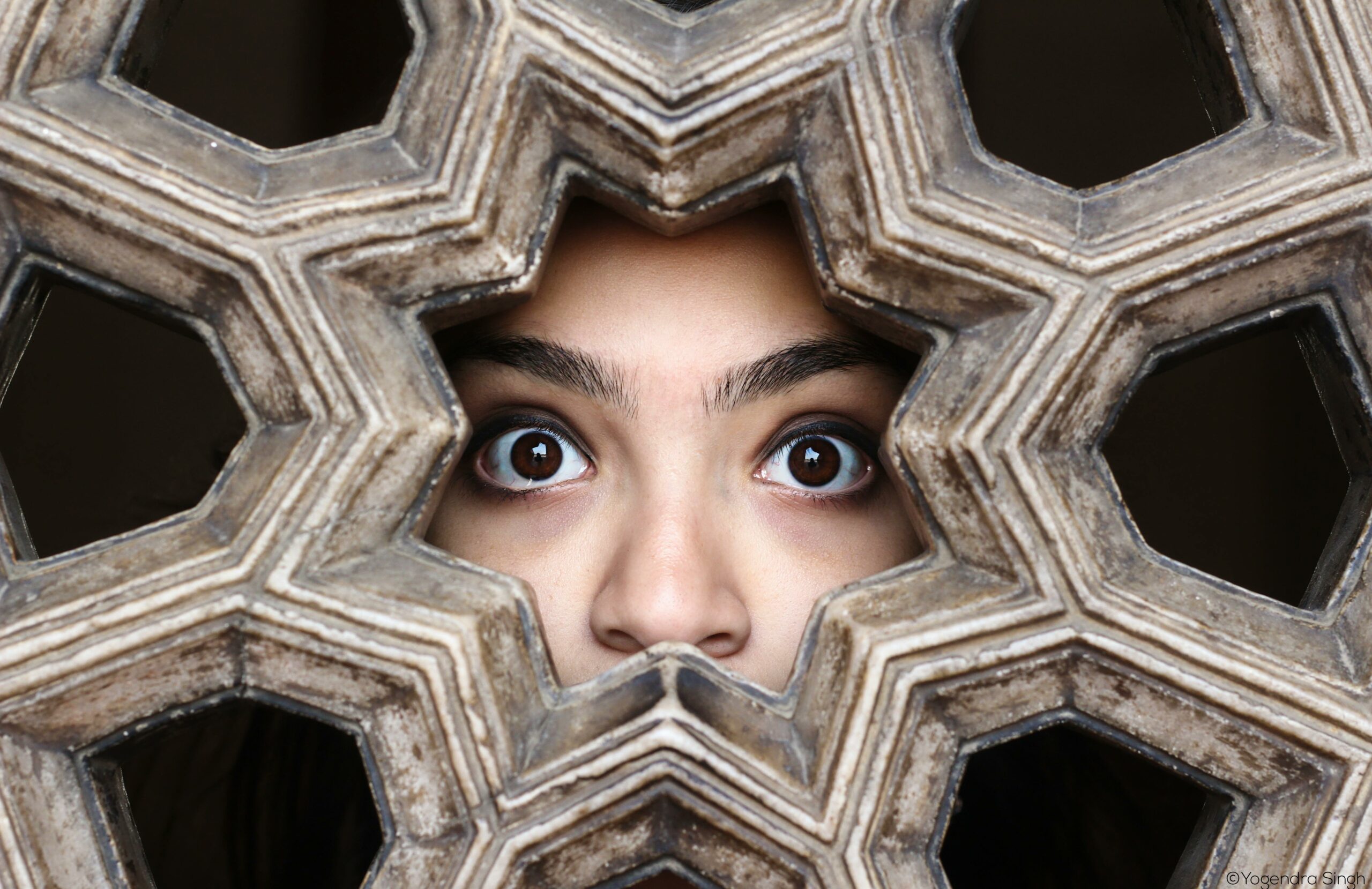Close-up of a woman's eyes peering through a decorative lattice in New Delhi, India.