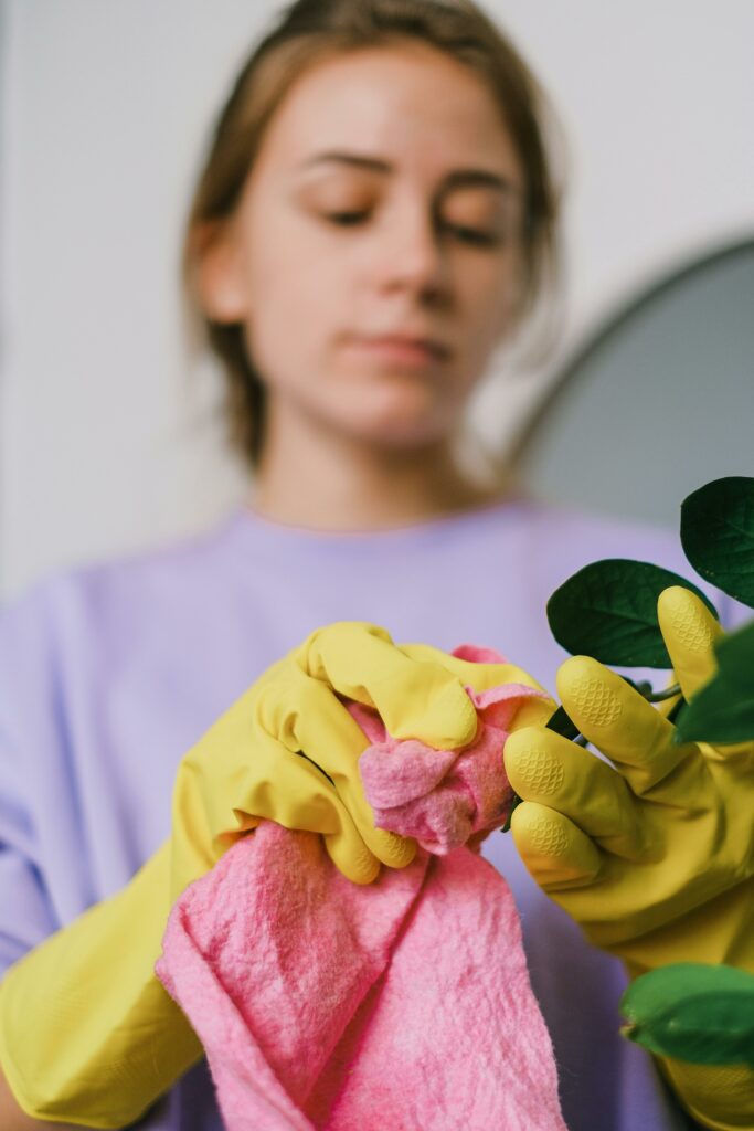 Focused woman in gloves cleaning with a pink towel indoors, emphasizing cleanliness and care.