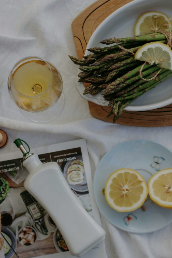 A sophisticated setup featuring asparagus with lemon slices, olive oil, and wine on a table.