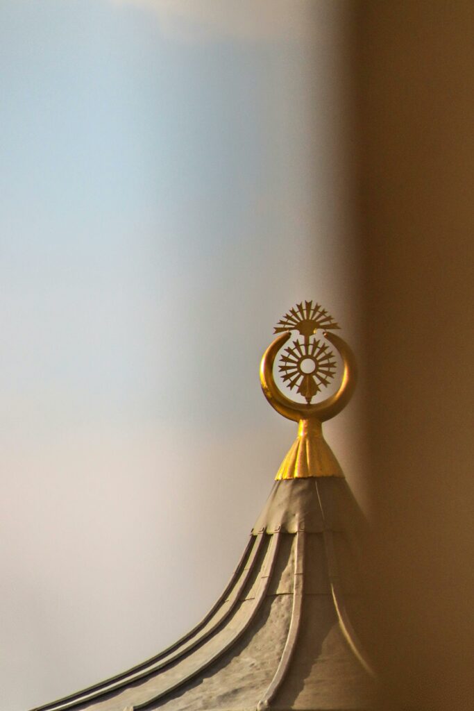 Close-up of a golden ornament atop a traditional roof set against a clear blue sky.