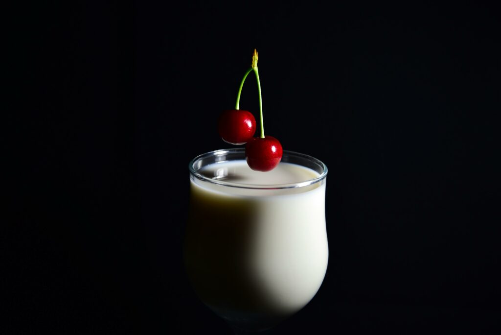 Minimalist shot of a milk glass garnished with cherries against a dark background, highlighting modern elegance.
