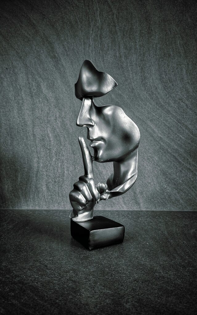 An abstract silenced face sculpture on a stone backdrop symbolizing secrecy and mindfulness.