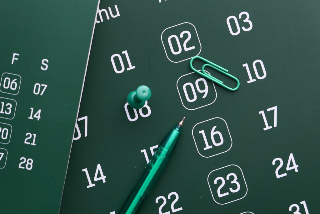 Close-up of a green calendar with pen, push pin, and paper clip for planning and organization.
