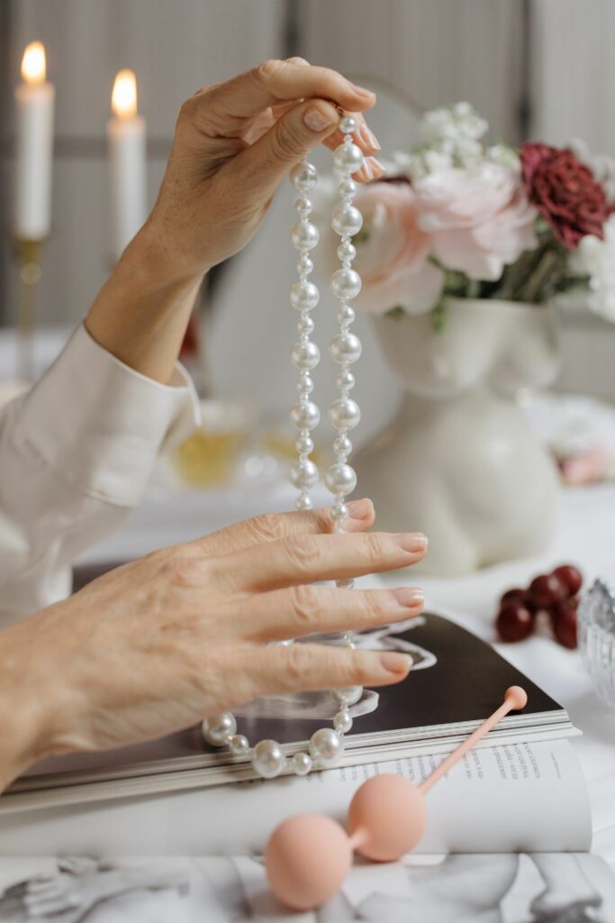 A woman elegantly holding a pearl necklace, surrounded by candles and a floral arrangement, creating a luxurious ambiance.