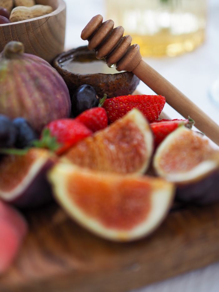 A close-up view of fresh figs, strawberries, and honey on a wooden board. Perfect for healthy eating concepts.