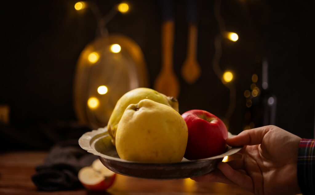 A rustic composition featuring apples and quince illuminated by warm fairy lights indoors.
