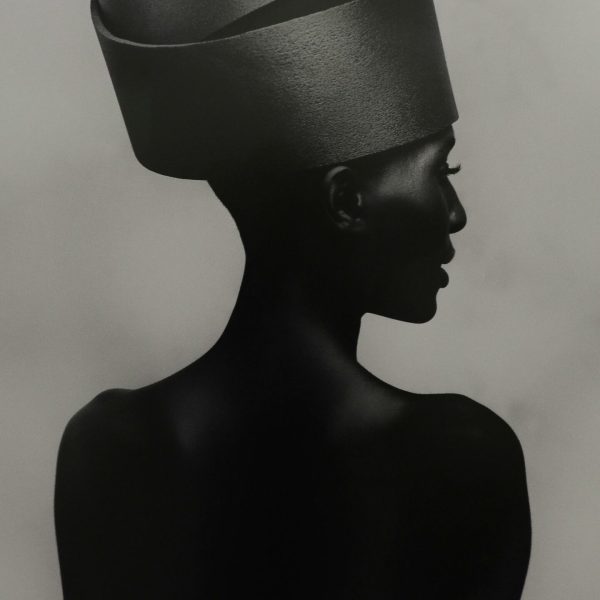Artistic studio shot of a woman wearing a modern, futuristic hat, captured in silhouette.
